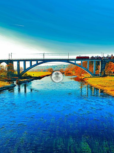 Anderswelt - Achat 2017 WEB Ein alter Zug fährt über eine Eisenbahnbrücke, die über einen Fluss führt. Ein warmer Herbsttag.